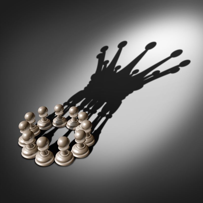 An arrangement of chess pawns forms a circular pattern on a gray surface, casting a shadow that resembles a star-like cluster.