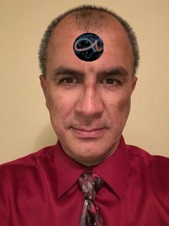 Un hombre con camisa roja y corbata oscura, con un símbolo que representa una de las constelaciones de Mazzaroth en la frente, de pie sobre un fondo liso.