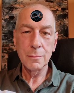 An elderly man with a solemn expression, featuring a sticker with a symbol from the Mazzaroth on his forehead, set against a blurred abstract background.