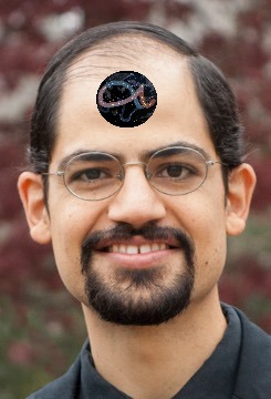 A smiling man with glasses and a neatly trimmed beard. He wears a black shirt, and a circular representation of the Mazzaroth is placed on his forehead, featuring a starry sky.