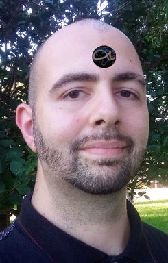 Un retrato de un hombre sonriente con un símbolo del Mazzaroth en la frente, de pie frente a un exuberante follaje verde.