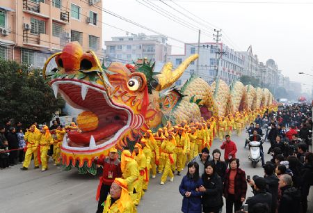A large, colorful dragon puppet paraded down a street by numerous people in yellow costumes, surrounded by spectators, symbolizing the Mazzaroth's fifth constellation.
