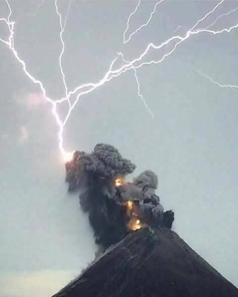 A dramatic scene featuring a volcano in the midst of eruption with a powerful lightning strike illuminating the ash-covered sky.