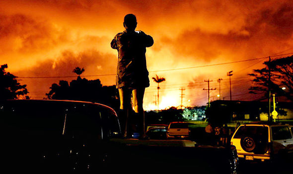 Silhouette of a person standing on a vehicle in a parking area, observing the celestial phenomena in the sky which displays a vibrant orange hue, reminiscent of the fiery Mazzaroth.