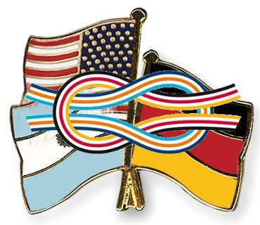 Two crossed flag pins, one depicting the United States flag and the other representing Germany's flag, with a multi-colored, ribbon-like pattern intertwining between them symbolizing unity and connectivity.