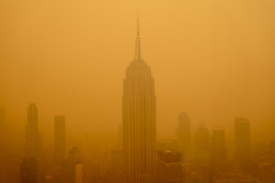 A city skyline shrouded in a dense golden haze, with a prominent skyscraper at the center under a murky sky.