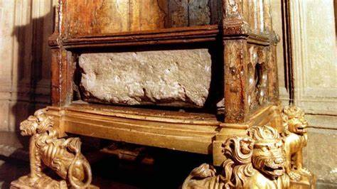 An ancient stone slab embedded with faded inscriptions, mounted on a gold-painted wooden frame supported by ornate lion sculptures. The setting suggests historical significance and possible religious or commemorative use.
