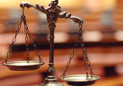 Close-up of a balanced scale with two symmetrical pans hanging by chains, set against a background of blurred wooden panels, symbolizing the astronomical constellation often associated with the Mazzaroth.