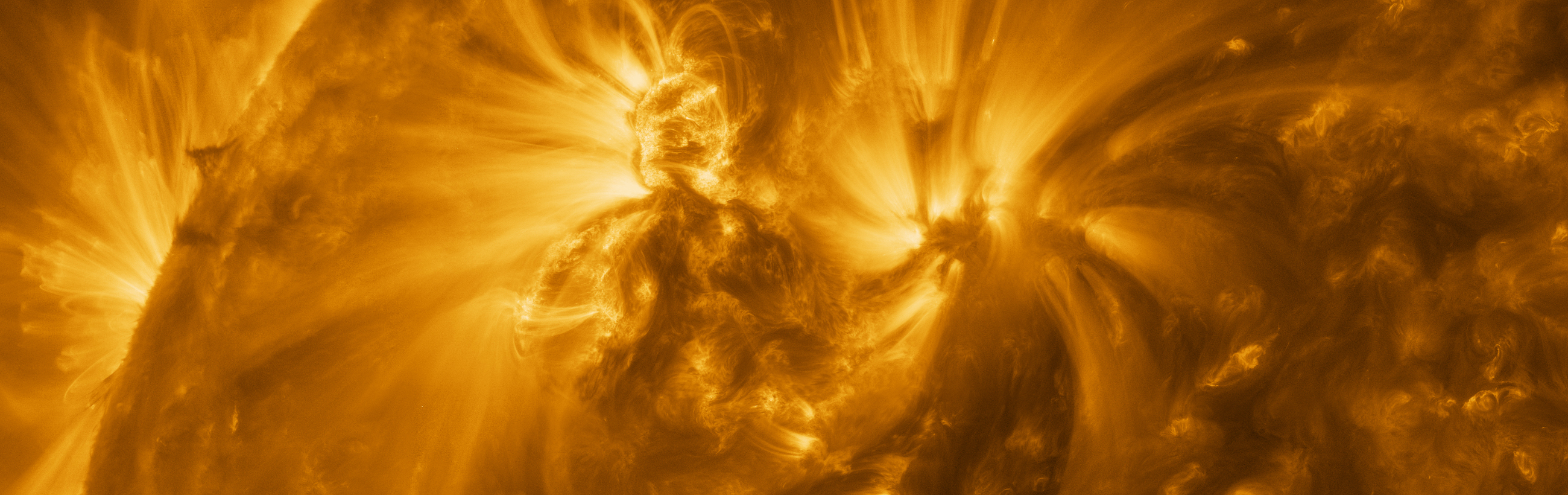 A panoramic view of dynamic solar activity captured in high resolution, showcasing a vibrant expanse of writhing solar material in golden hues with a bright, expansive solar flare at the center.