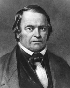 Black and white portrait of a middle-aged Caucasian man with a stern expression, wearing a dark jacket, white shirt, and bow tie. He has short, side-parted hair and notable jowls.