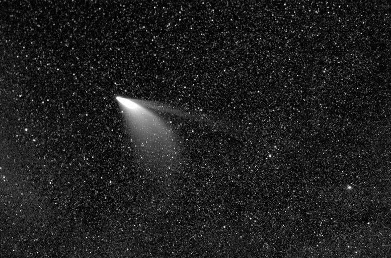 A celestial comet with a glowing nucleus and elongated tail is prominently featured amid a field of numerous stars in a dark sky.