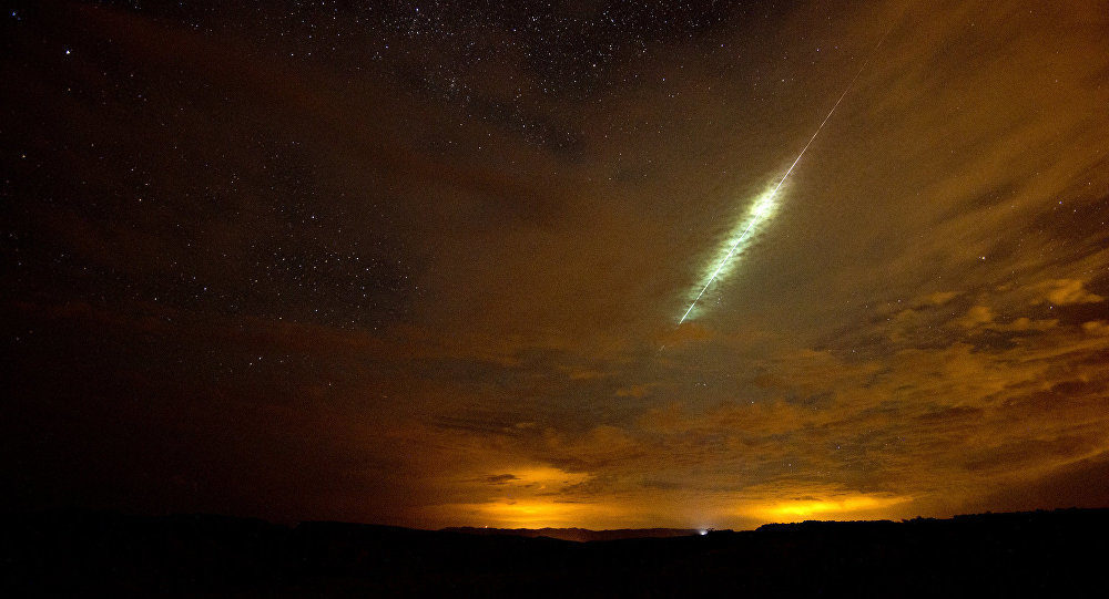 A meteor streaking through a star-filled night sky over a landscape softly illuminated by distant city lights, under a harmonious blend of natural celestial patterns.