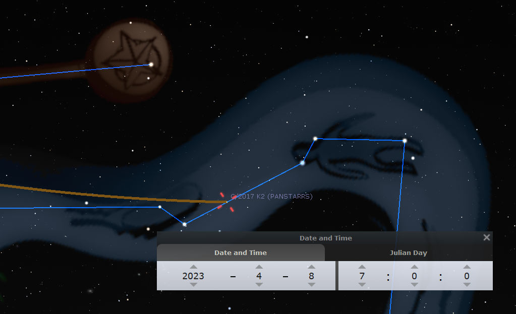 Digital astronomical simulation depicting a constellation from the Mazzaroth in the night sky, connected by blue lines forming a geometric shape. A date and time panel shows April 8, 2023. Visible are various stars and a comet labeled "2017 K2 (PANSTARRS)" with its trajectory marked by lines. A coin-like object with a pentagram is shown in motion near the comet.