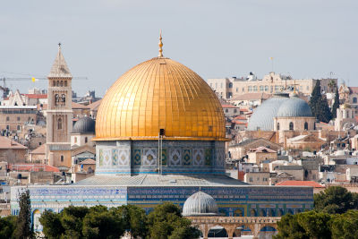 A panoramic view featuring the golden dome of the Dome of the Rock against a cityscape, under a clear sky.