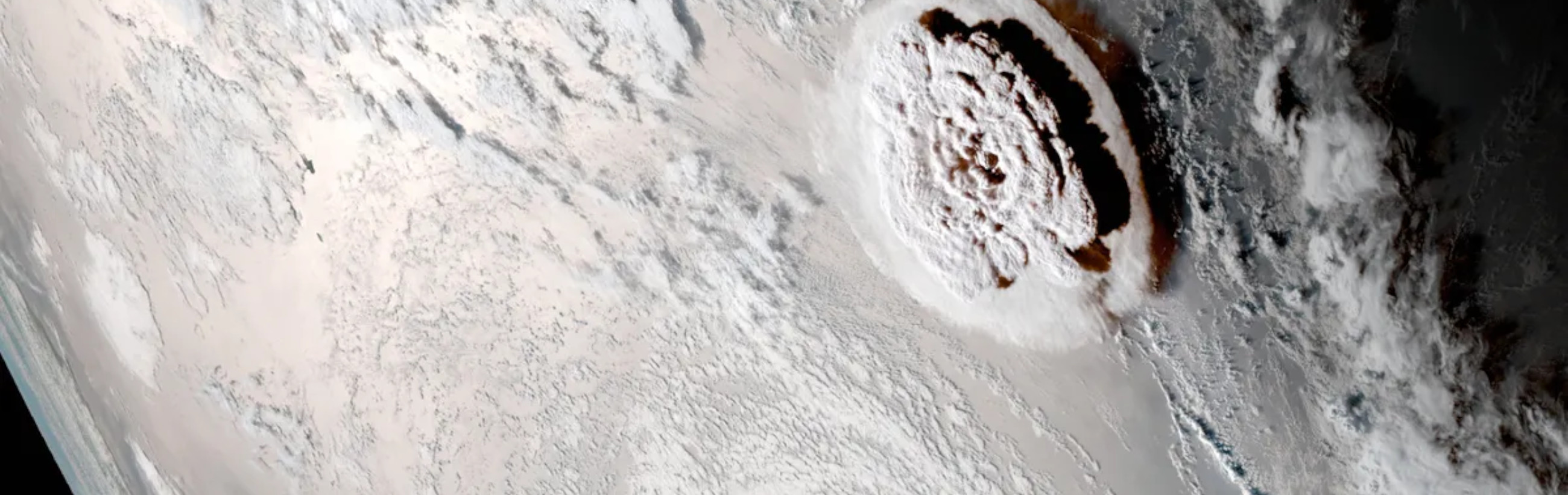 A satellite image showing a large, detailed circular cloud formation with intense swirl patterns, resembling a rose, centered over an icy landscape. The surrounding areas are covered with a mixture of clouds and snow, creating a stark contrast of white against the darker sea and land masses.