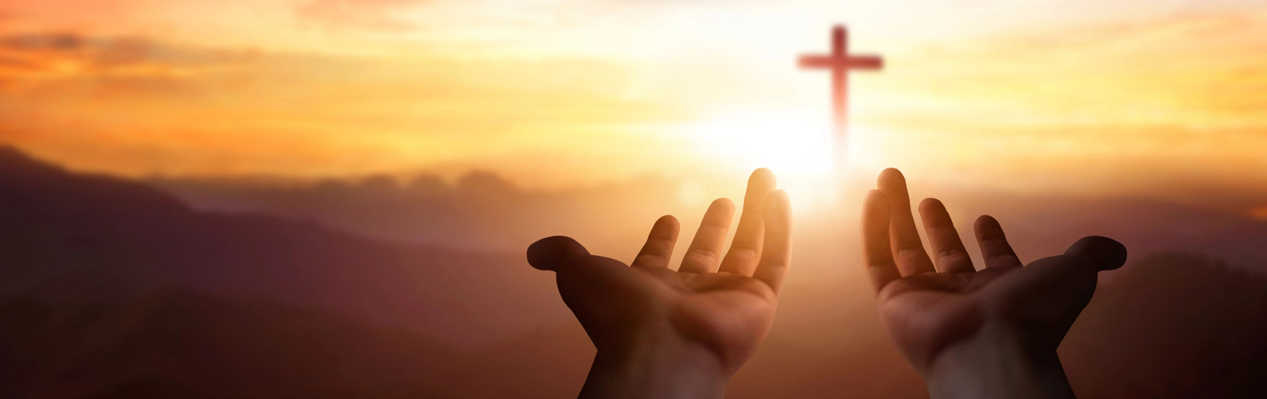 Two open hands are extended towards a radiant sunrise that illuminates a silhouette of a cross standing resolutely on a distant hilltop, symbolic of faith and hope amidst the luminescence of dawn's early light.