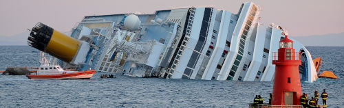 Una escena de rescate marítimo muestra un gran crucero considerablemente inclinado en aguas oceánicas cerca de un afloramiento rocoso, con un faro rojo en primer plano. Un bote de rescate se encuentra junto al barco, y el personal de emergencia observa desde la orilla.