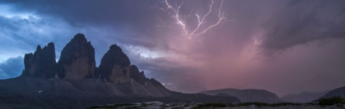 Una vista panorámica de una escena climática dramática con picos de montañas irregulares bajo un cielo crepuscular, que presenta una sorprendente exhibición de relámpagos y un brillo suave que podría evocar las luces menores del cielo, contra una formación de nubes amenazante.