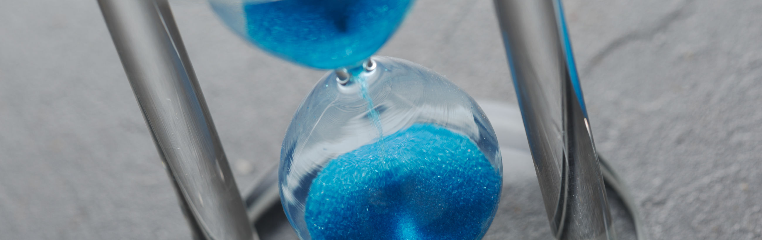 Close-up of a blue sand hourglass capturing the flow of time, depicting the continuous cycle reminiscent of celestial orbits.