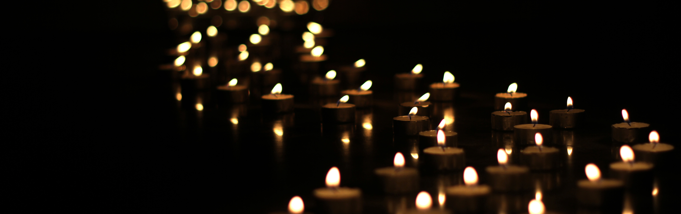 A serene arrangement of numerous small candles with flickering flames, set against a deep black background, creating a celestial representation akin to stars scattered across the night sky.