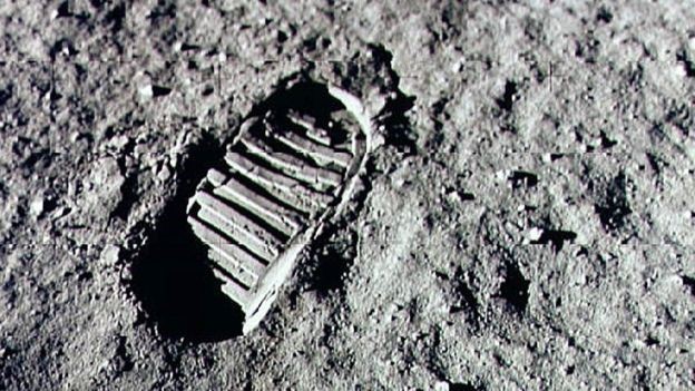 Close-up image of a human boot imprint on a fine, gray, lunar soil surface, symbolizing human exploration beyond Earth.