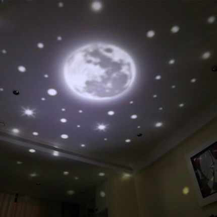 An indoor projection displaying a luminous full moon surrounded by numerous bright stars against a dark ceiling, evoking the night sky.