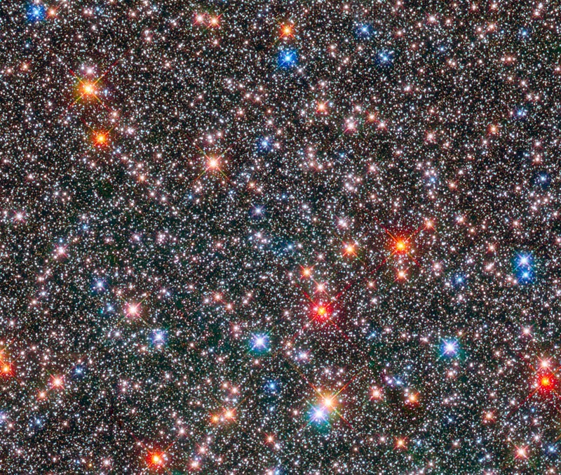 A vibrant celestial field displaying thousands of stars of various sizes and colors, from intense blue to vivid red set against a dense backdrop of smaller, fainter stars, illustrating the vastness and variety of the universe.