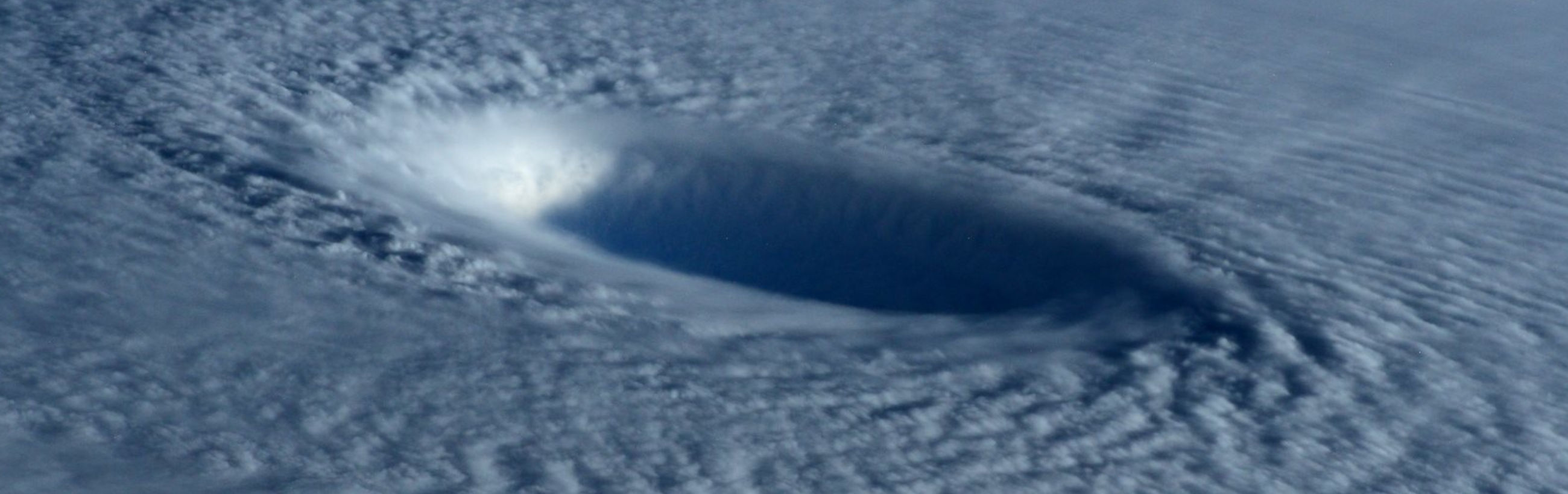An aerial view of a large, deep blue atmospheric vortex amidst white cloud cover, illustrating dynamic air movements in Earth's atmosphere.