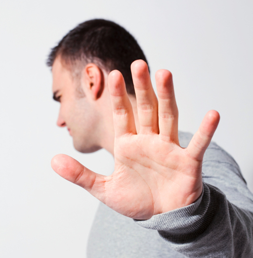 Side view of a man extending his left hand towards the camera in a halting gesture, palm visible and fingers spread, with a neutral background.