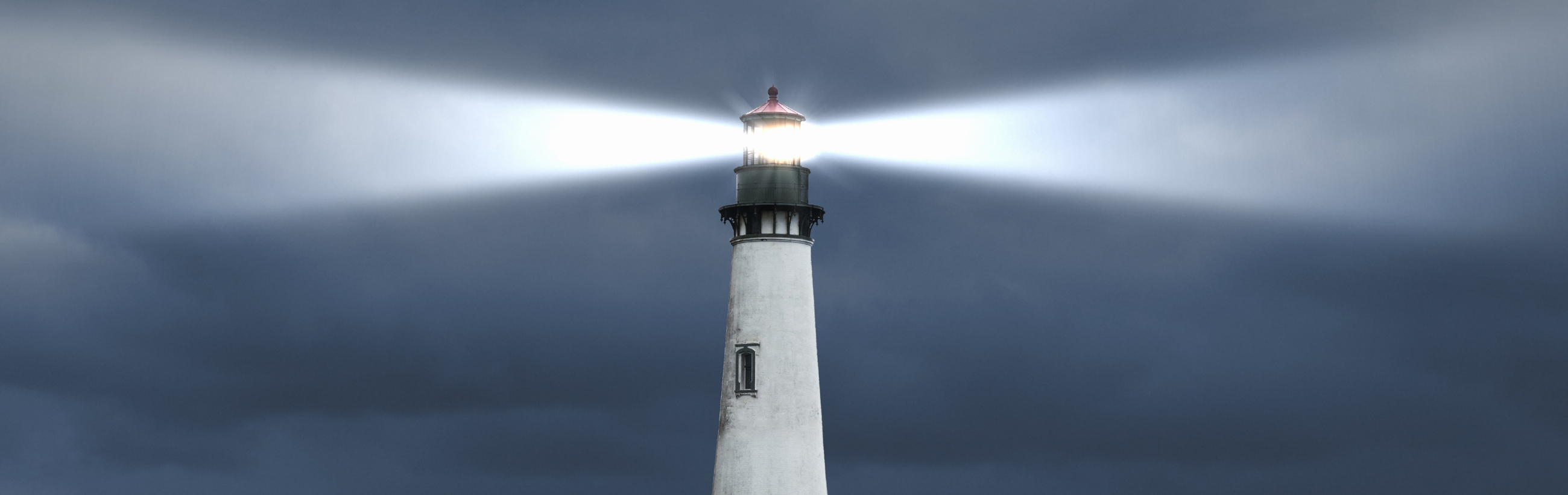 A panoramic image of a tall white lighthouse emitting a bright beam of light, piercing through a dark and stormy sky.