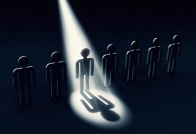 A graphical representation featuring a lineup of eight stylized human figures in a dark setting, with one figure centrally illuminated by a beam of light casting a distinct shadow.