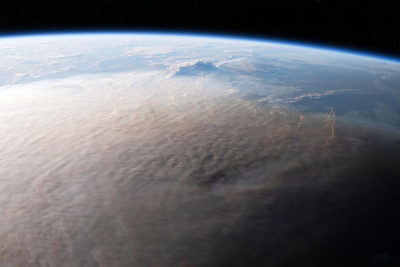 View of Earth from space showing a curved horizon and clouds covering the terrestrial surface, with a glimpse of blue sky and darkness of space above.
