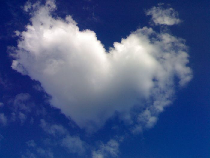 A single cloud shaped like a heart against a vivid blue sky, surrounded by smaller wisps of clouds, symbolizing a unique and ephemeral creation in the heavens.