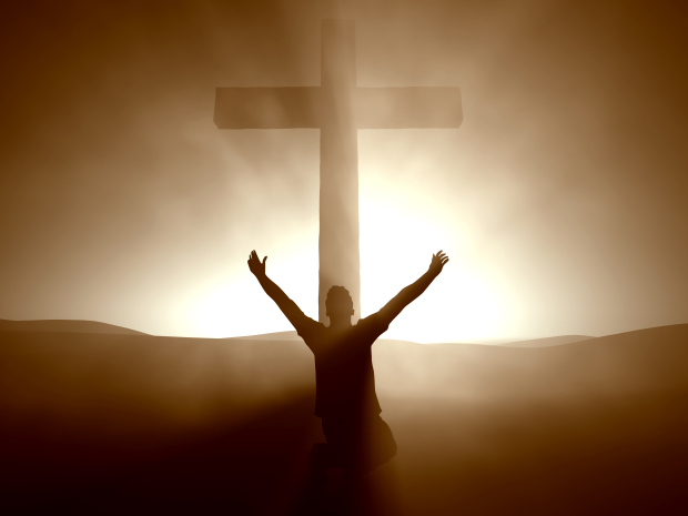 A silhouette of a person with arms raised in worship, kneeling before a large cross, set against a radiant, glowing background.