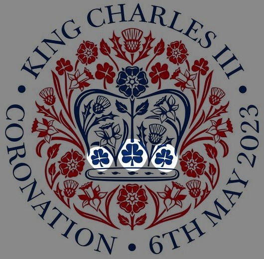 A circular emblem featuring a central crown surrounded by a ring of red and blue floral designs. The crown, in blue, sits atop a symmetrical arrangement of thistles, roses, and shamrocks, emblematic of celestial constellations. Text around the edge reads "King Charles III Coronation 6th May 2023."