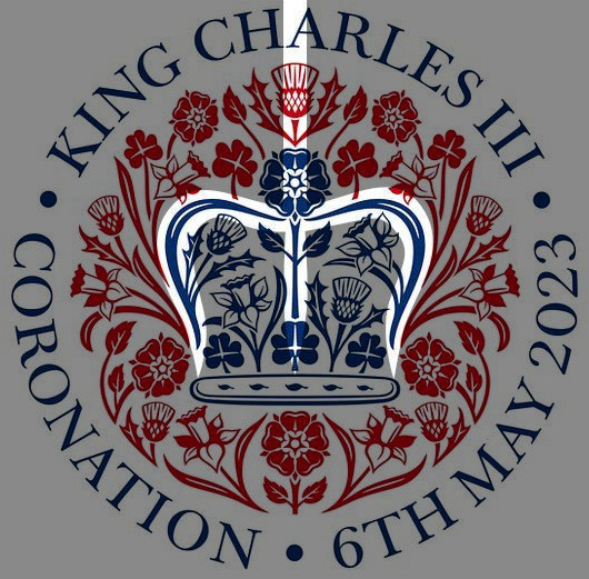 A ceremonial emblem featuring a stylized crown flanked by floral designs, centered within a circular frame. Text within the frame states "King Charles III Coronation 6th May 2023". The embellishments use shades of red, blue, and white.