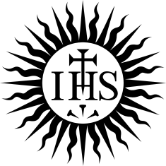 Monochrome emblem featuring the letters "IHS" in a stylized font, overlaid on a circular white background, surrounded by black. Below the letters, there is a three-pointed shape resembling an abstract depiction of a manger or a simple crown.