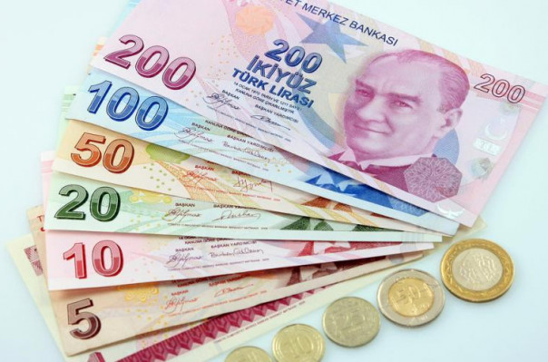 An assortment of Turkish Lira banknotes in various denominations spread out, with coins also visible. The banknotes are colorful, featuring different vibrant hues and the portrait of Mustafa Kemal Atatürk.