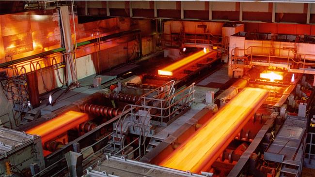 A steel mill interior with glowing molten metal rods being processed. The scene is illuminated by the intense orange light emitted from the hot metal, creating a stark contrast with the darker areas of the facility.