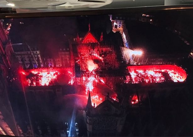 Aerial nighttime view of an illuminated architectural structure with intense red lighting resembling a celestial phenomenon. The lights cast a vivid glow over ornately designed buildings, creating a dramatic and mysterious ambiance.