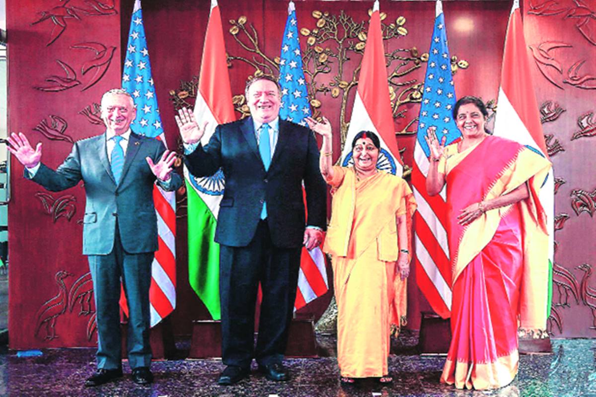 Four diplomats stand waving in front of a backdrop featuring an assortment of national flags and symbolic designs, including a depiction resembling a tree and various stylized animals but avoiding direct reference to the Mazzaroth. Three men are in suits, and one woman in a brightly colored sari.