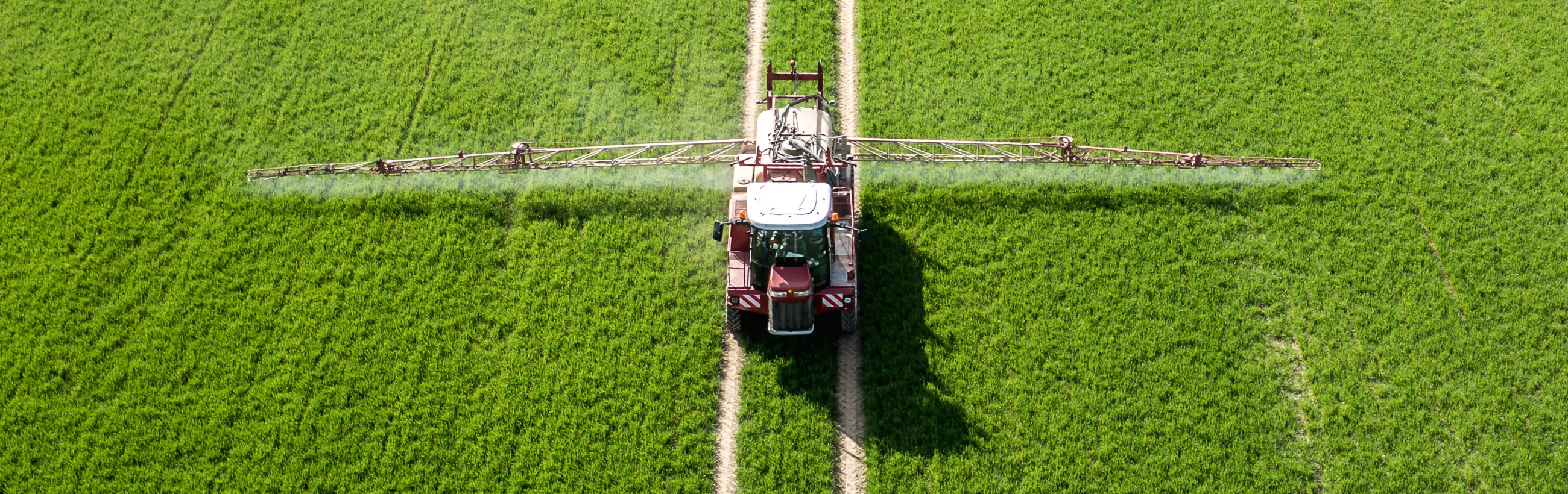 Aerial view of a crop sprayer applying treatments on a verdant field, marking a stark contrast in the greenery with its track lines.