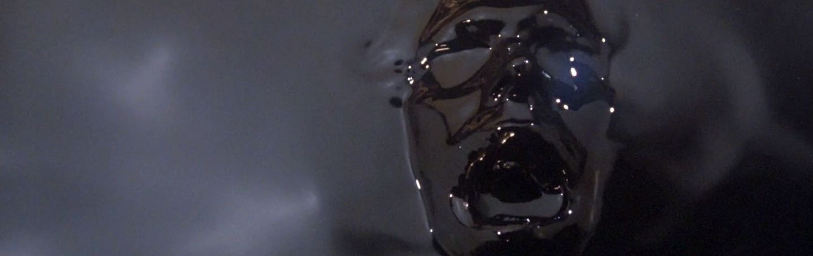 A reflective, metallic surface shaped like a human face distorts light and surroundings, offering a glimpse of cosmic shimmer reminiscent of reflections seen on the waters under the heavens.