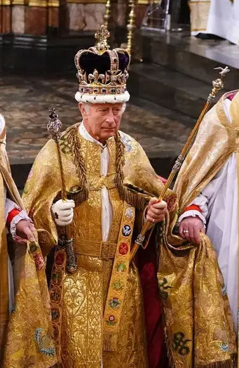 A dignified elder man wearing a grand golden robe adorned with elaborate embroidery and symbols, some reflective of the Mazzaroth. He stands solemnly with a jeweled crown on his head, holding a scepter in one hand and an orb in the other.
