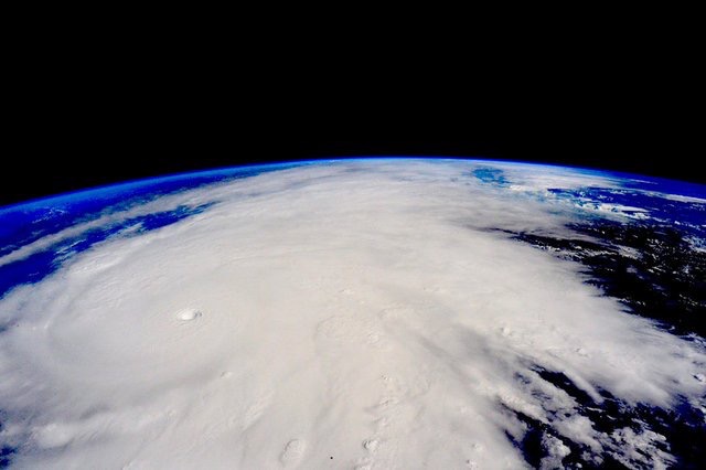 View of a large cyclonic storm from outer space, showcasing swirling clouds around a distinct eye, with the curvature of the Earth visible on the horizon.