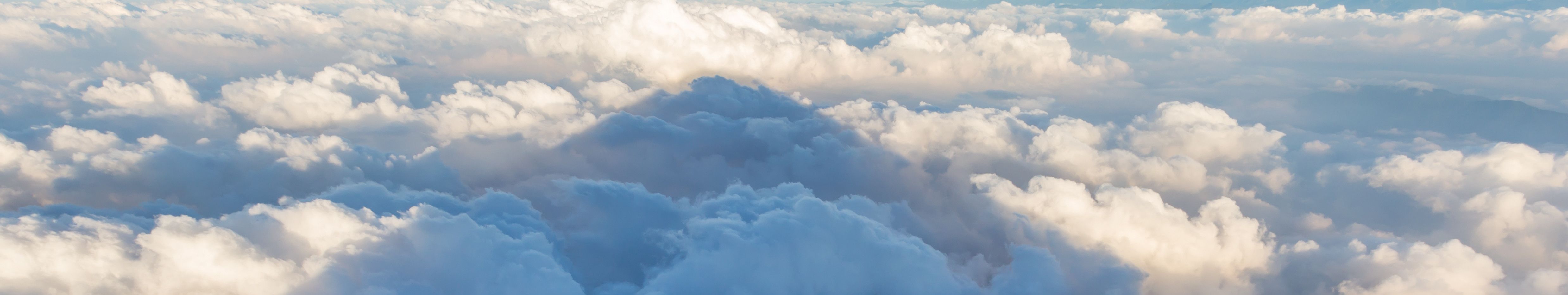 Expansive view of billowing cloud formations illuminated by sunlight, showcasing subtle shades of blue and white with hints of golden light penetrating through, suggesting the grandeur of the creation depicted in the firmament.