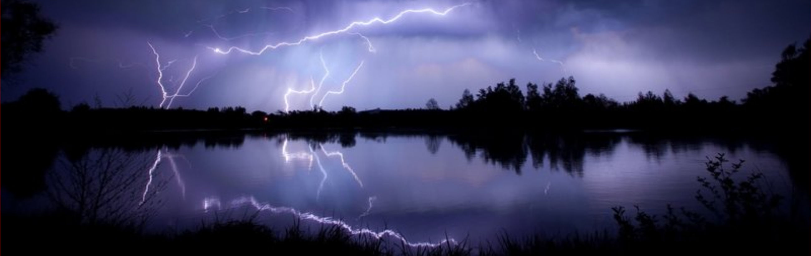A nighttime scene depicts a vivid display of lightning arcing through the heavens, reflected in a tranquil lake below, surrounded by silhouetted foliage and trees under a shadowy sky.