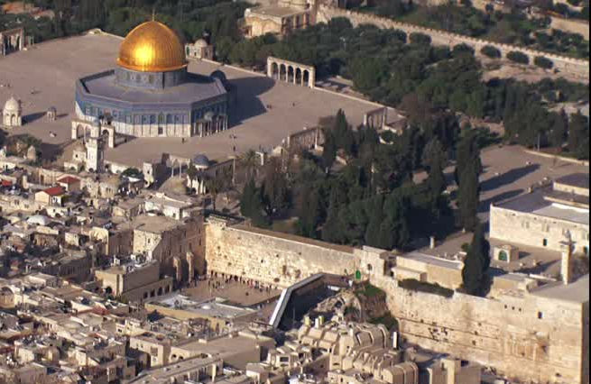Aerial view of a historical cityscape featuring a prominent golden-domed structure surrounded by green trees and numerous densely packed buildings.