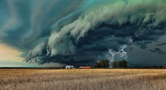 A dramatic thunderstorm rolls across a rural landscape, with ominous dark green clouds enveloping the sky above golden fields. Lightning strikes illuminate the scene near a small cluster of farm buildings.