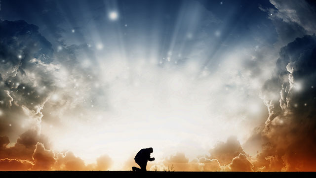 Silhouette of a person kneeling and praying on a hilltop at sunrise, with dramatic clouds and rays of sunlight illuminating the sky.